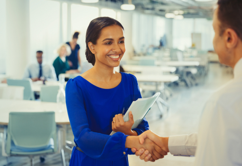 A young woman in a blue dress shaking hands with a gentleman and smiling
